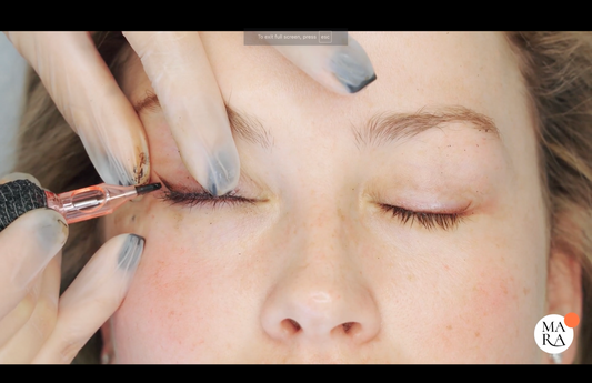 A person receiving eyeliner tattooing, eyes closed, with a hand applying the tattooing tool.