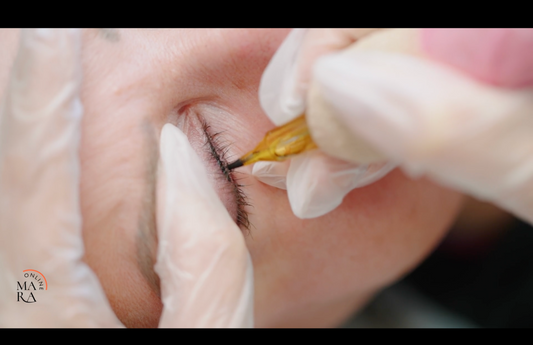 A close-up of a person applying eyeliner using a fine-tipped tool, with gloved hands.