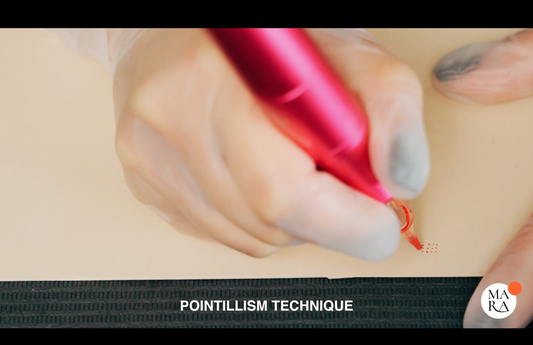 A hand holding a pink pen applies red dots on a light surface, demonstrating pointillism technique.