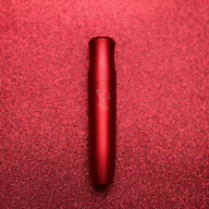 Red tube-shaped device with a matte finish, positioned on a sparkling red background.